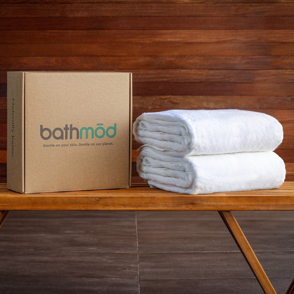 Two stacked white bath sheets on a wooden bench beside a box