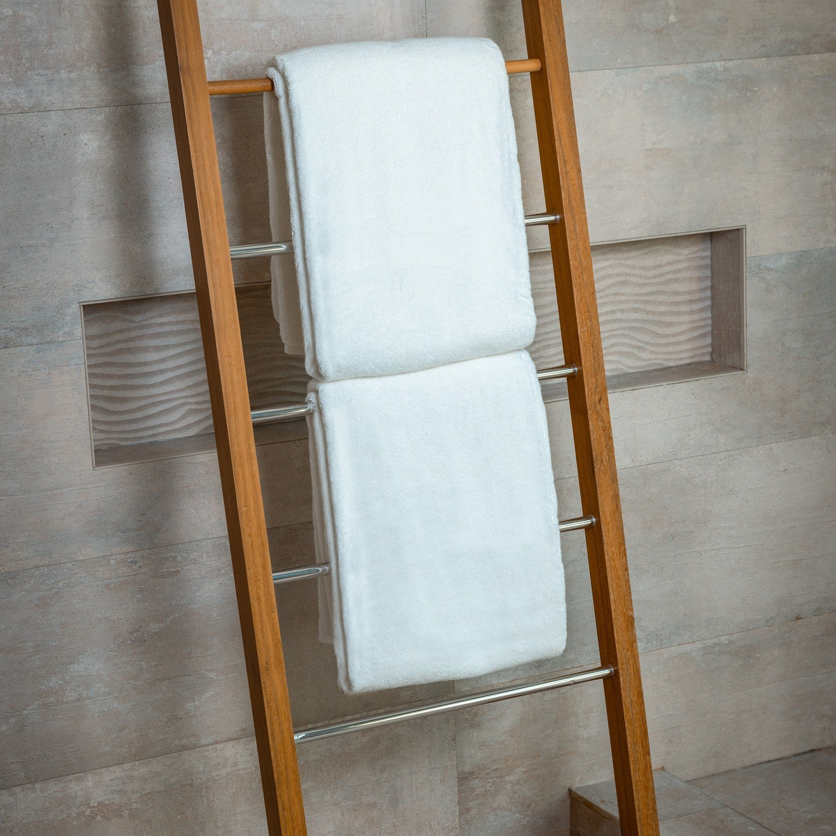 Two light blue bath sheets stacked on wooden ladder rack