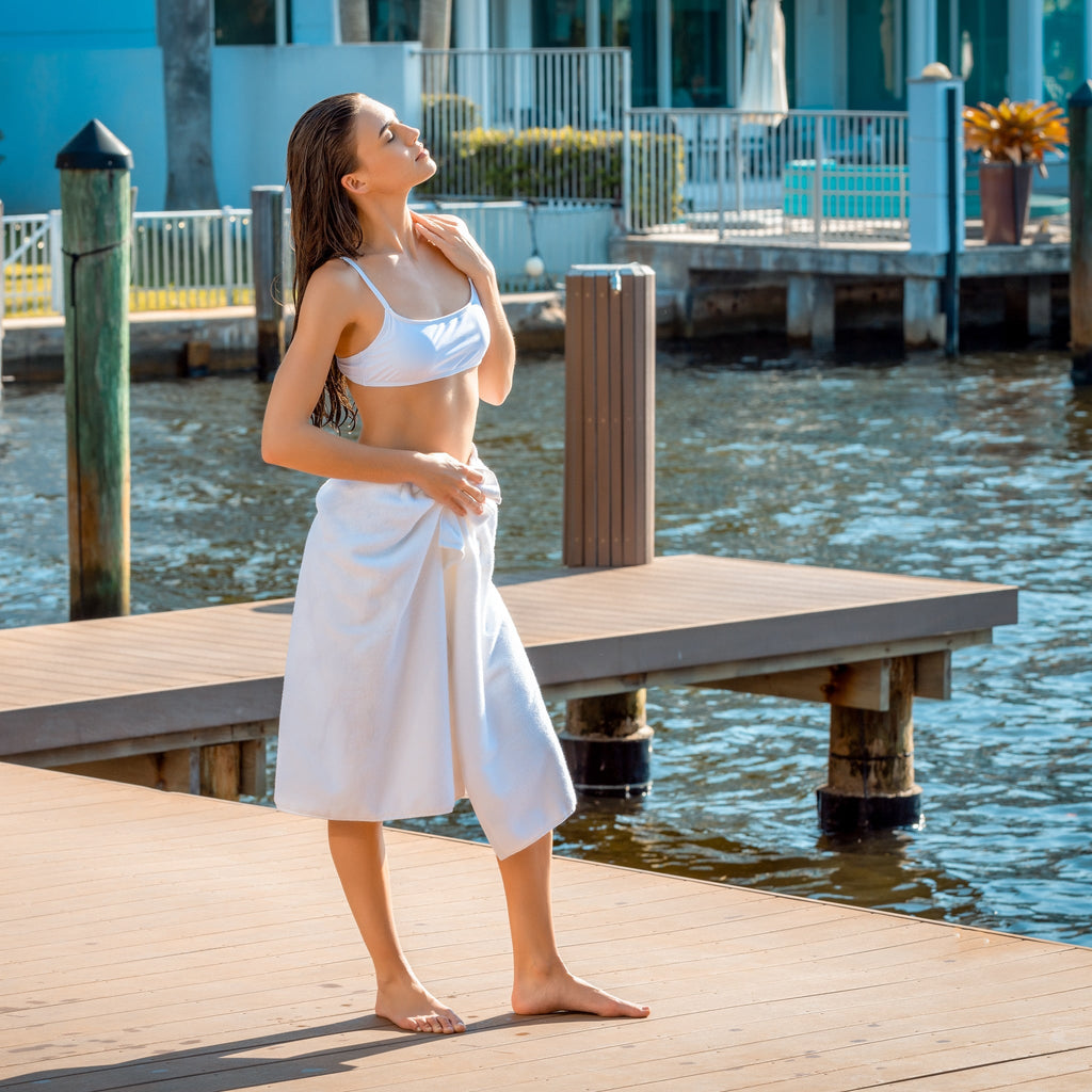 Person wrapped in a white bath sheet at a waterfront deck