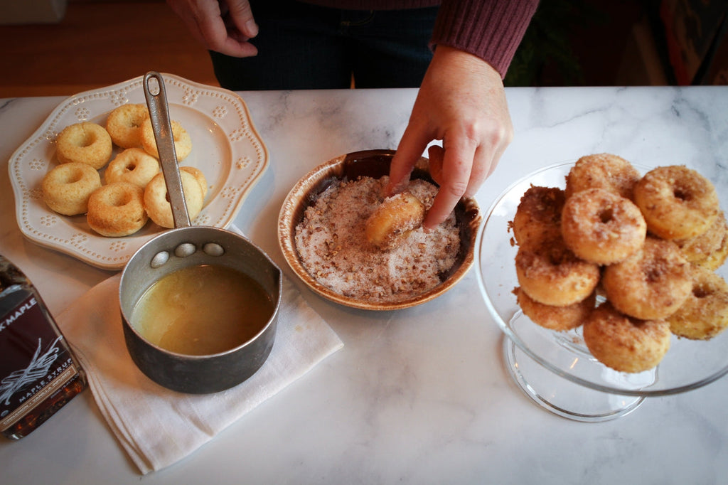 Metal cup of cinnamon-vanilla maple syrup beside pastries on plate