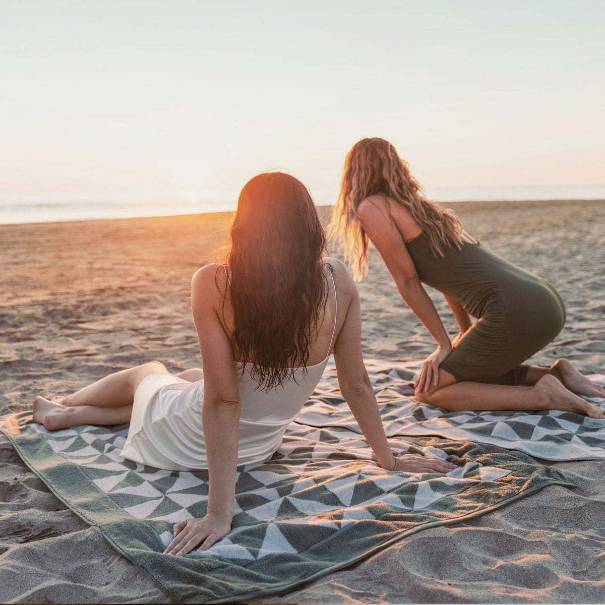 Sage green and ecru geometric cotton beach towels laid out on sand