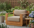 Outdoor teak wood armchair with beige seat and back cushions, wide arms and slatted frame.