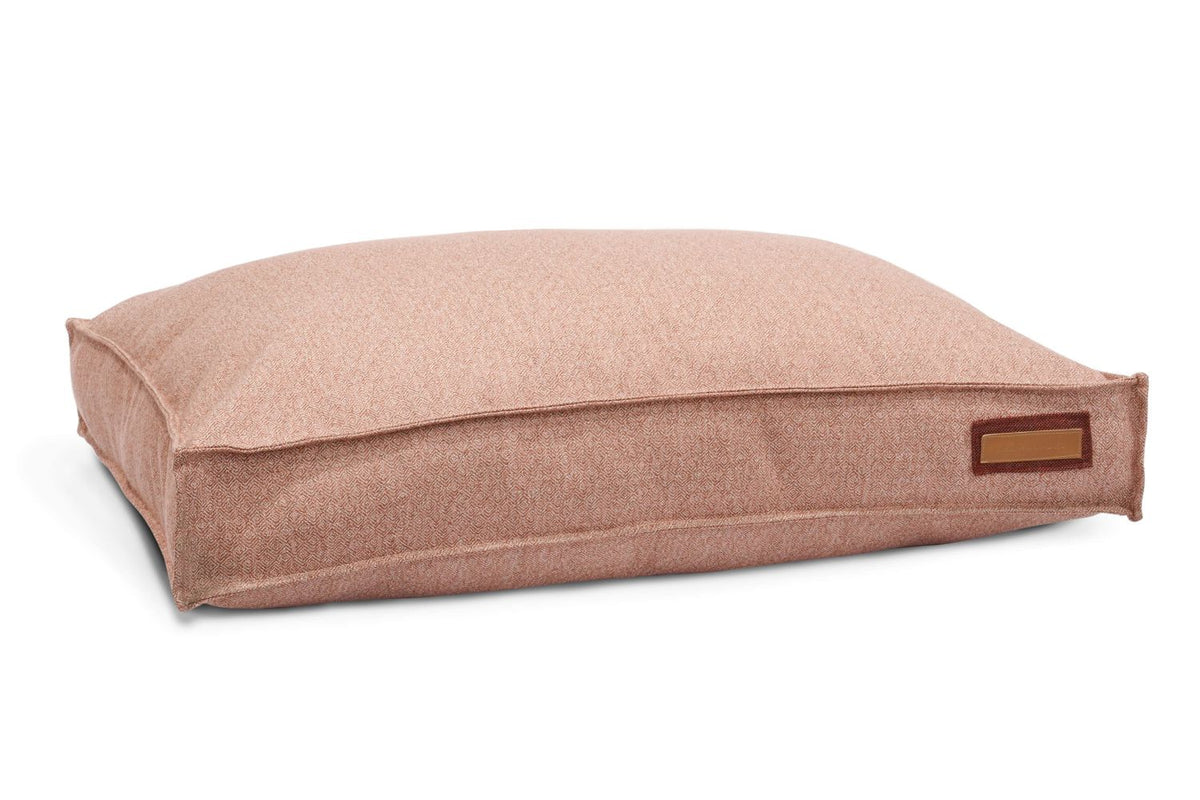 Dusty pink pet bed cushion in textured fabric with tan label, side view