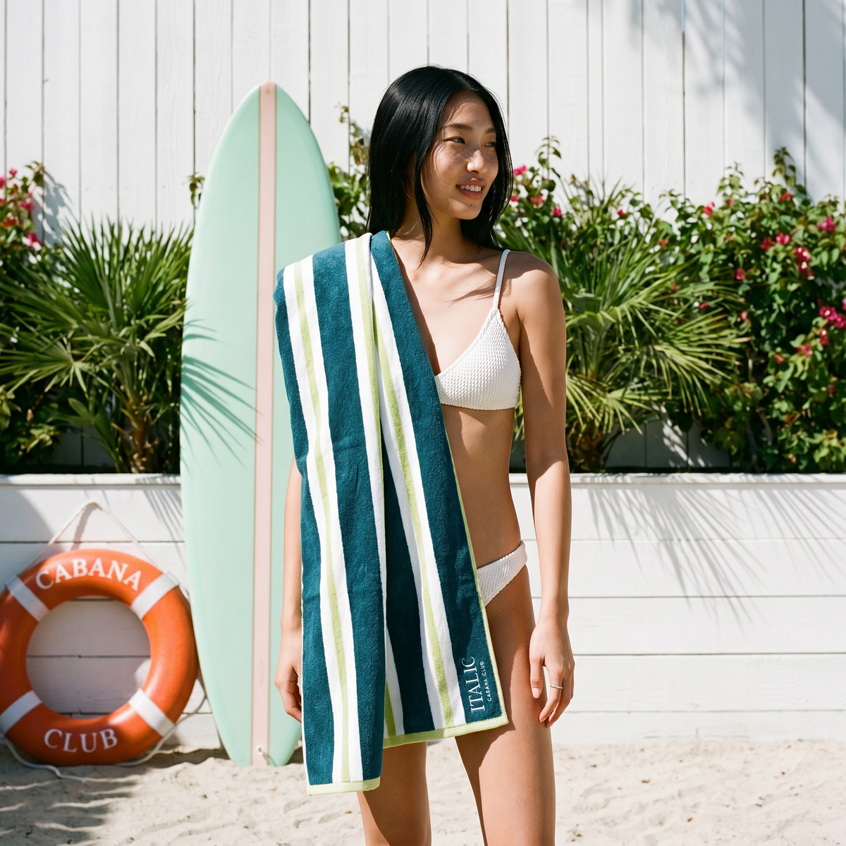 Teal and white striped cotton beach towel with terry texture, held by a person.