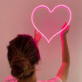 Pink heart neon wall hanging light with bright outline held up on a wall