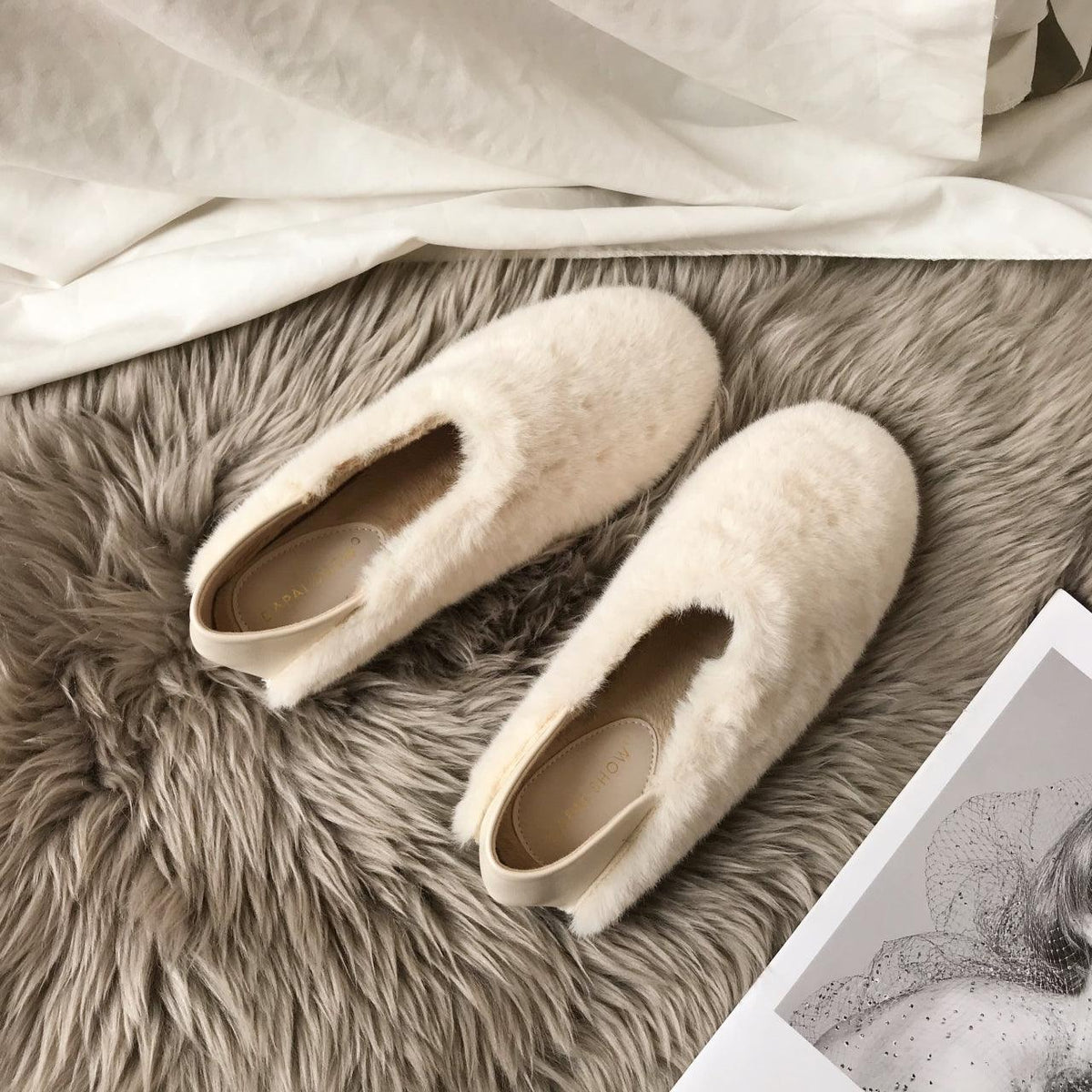 Cream white fuzzy round-toe slip-on loafers with tan footbed, pair on gray rug