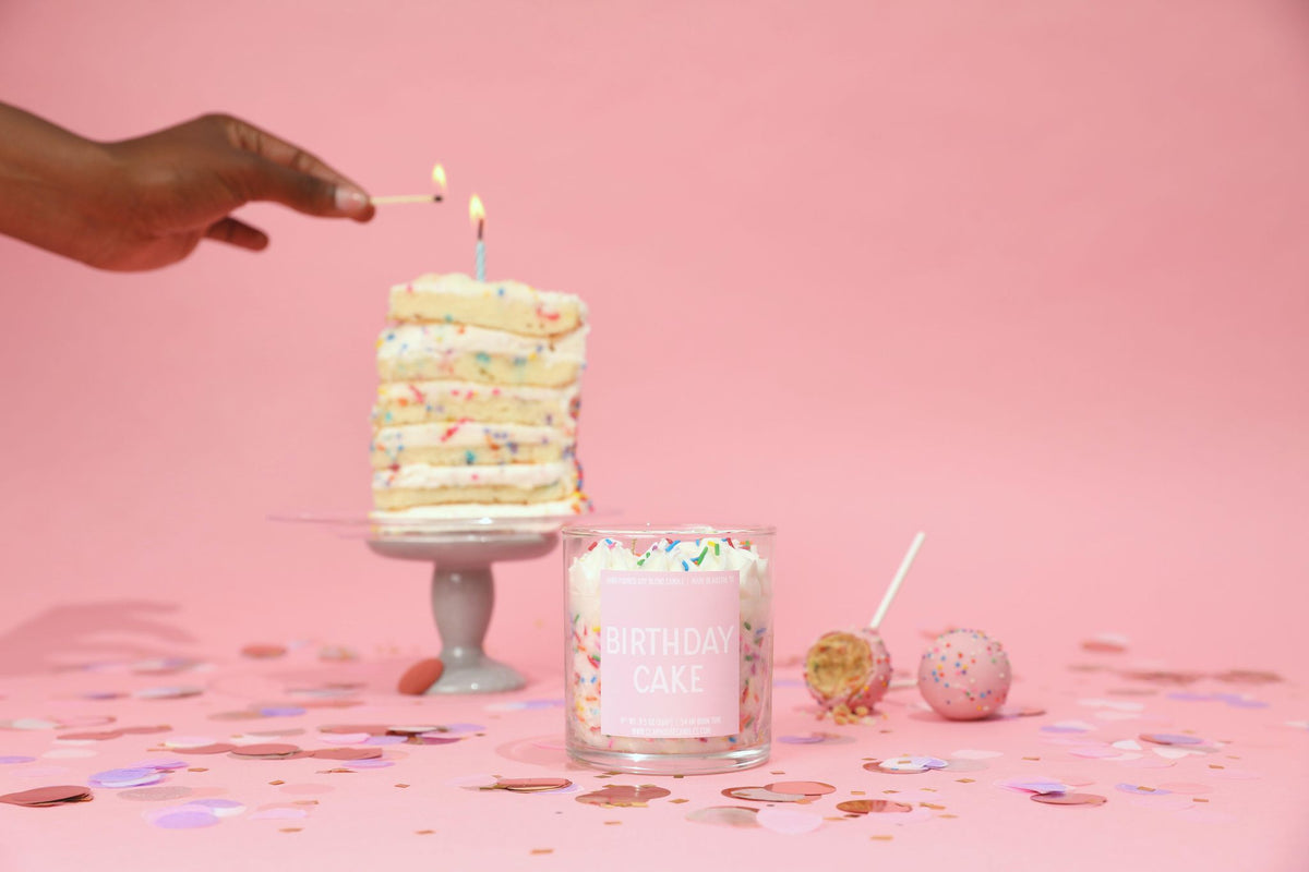 Lit cake-layer candle on stand and glass jar cake candle with sprinkles