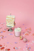 Cake-layer container candle with glass jar, colorful sprinkles and lit wick on stand