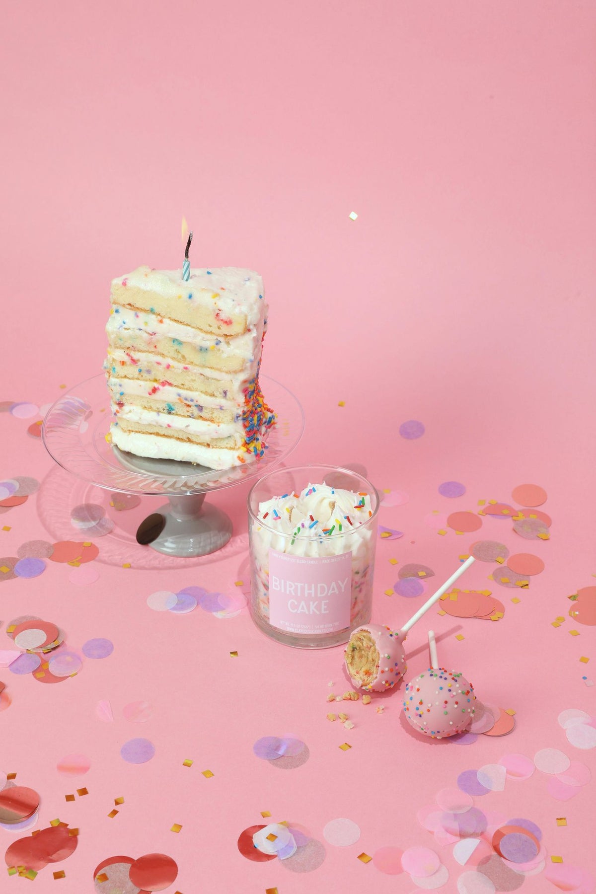 Cake-layer container candle with glass jar, colorful sprinkles and lit wick on stand