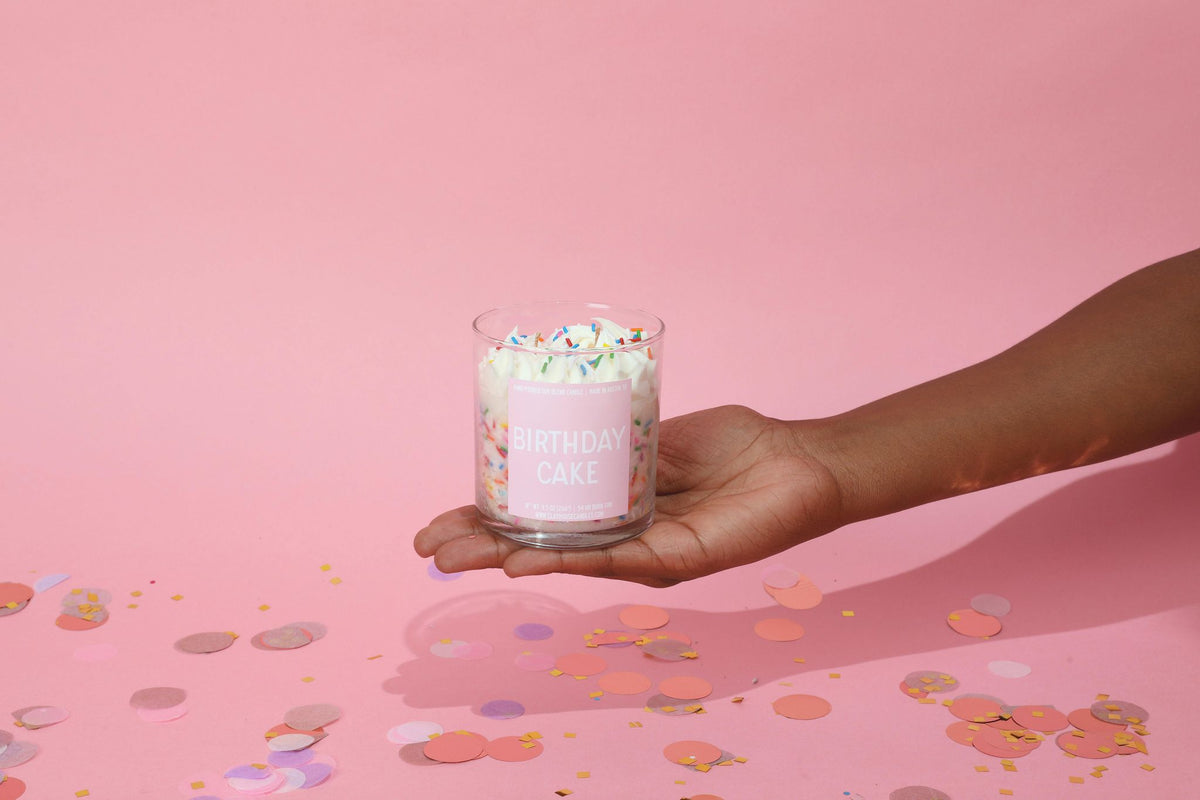 Glass jar cake candle with colorful sprinkles, held in a hand