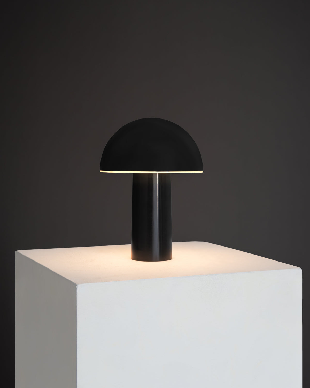 Black portable lamp with dome shade and glossy cylindrical base, warm light