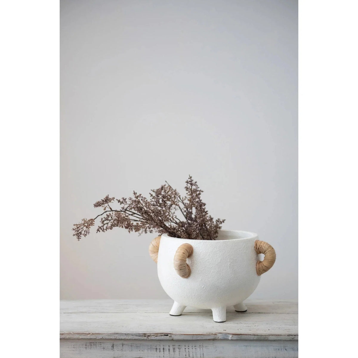 White planter with rattan side handles holding dried branches