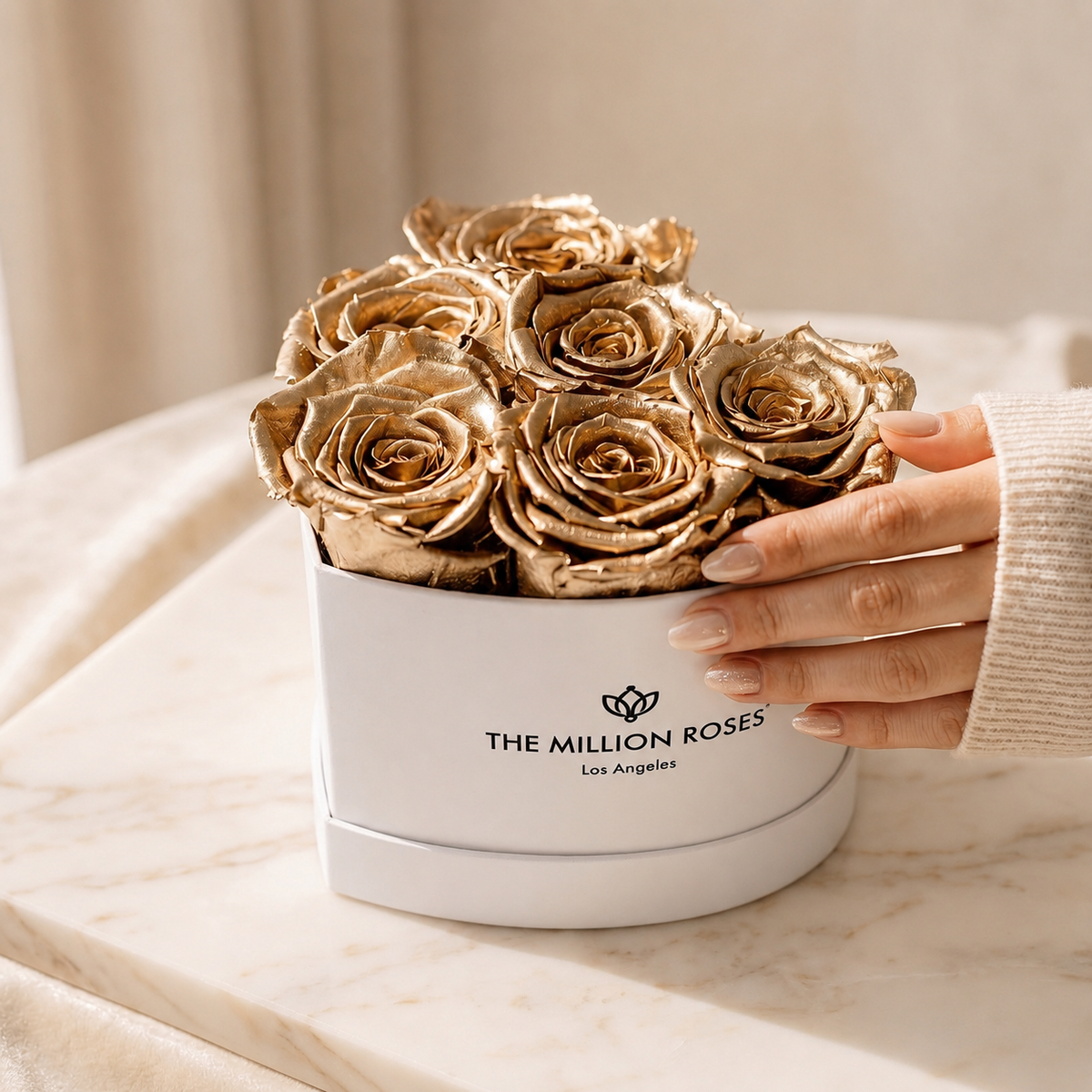 White round gift box of gold roses with hand adjusting the flowers; THE MILLION ROSES