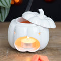 White ceramic pumpkin oil burner with star cutouts, lit candle in bowl
