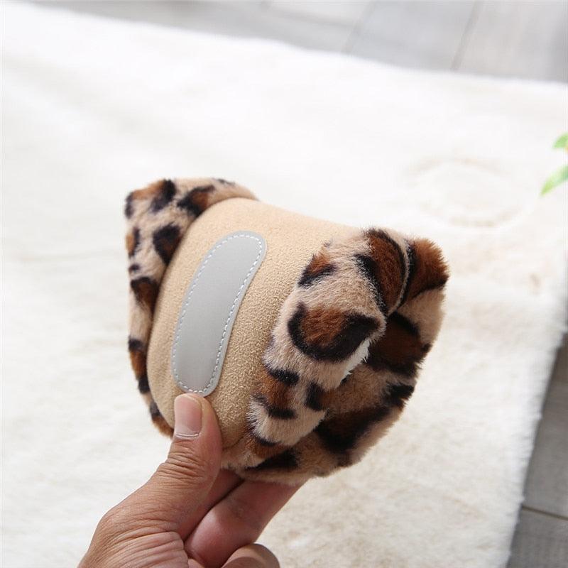Hand holding tan and brown leopard-print plush slip-on slipper