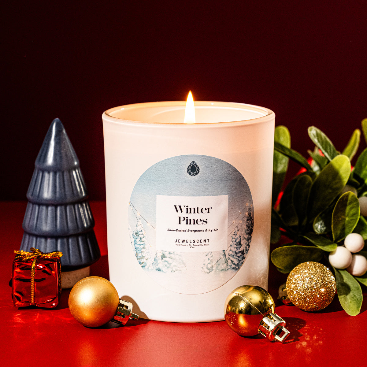 White candle in glass jar with Winter Pines label and burning flame