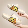 White slip-on slides with thick sole and cartoon face, shown being held by hands.