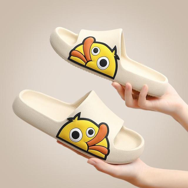 White slip-on slides with thick sole and cartoon face, shown being held by hands.