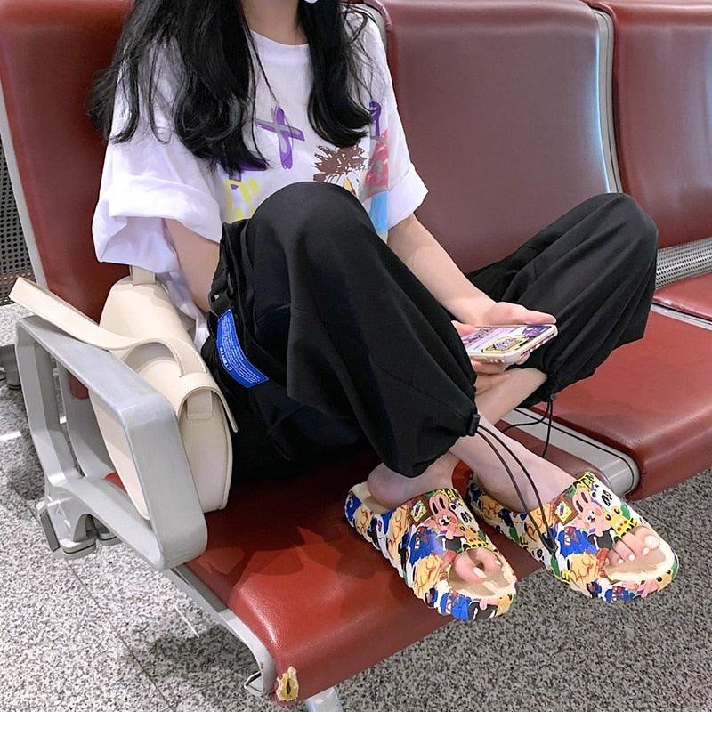 Cartoon slide sandals with multicolor character print, open toe on a seated person