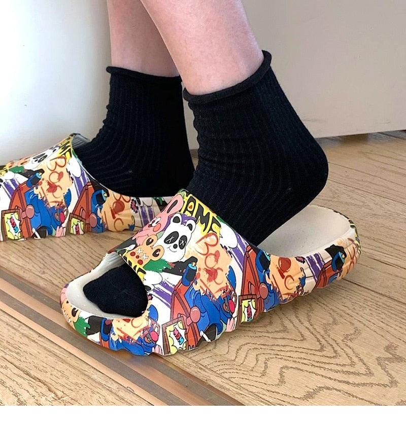 Multicolor cartoon slide sandals on feet with black ankle socks, open toe