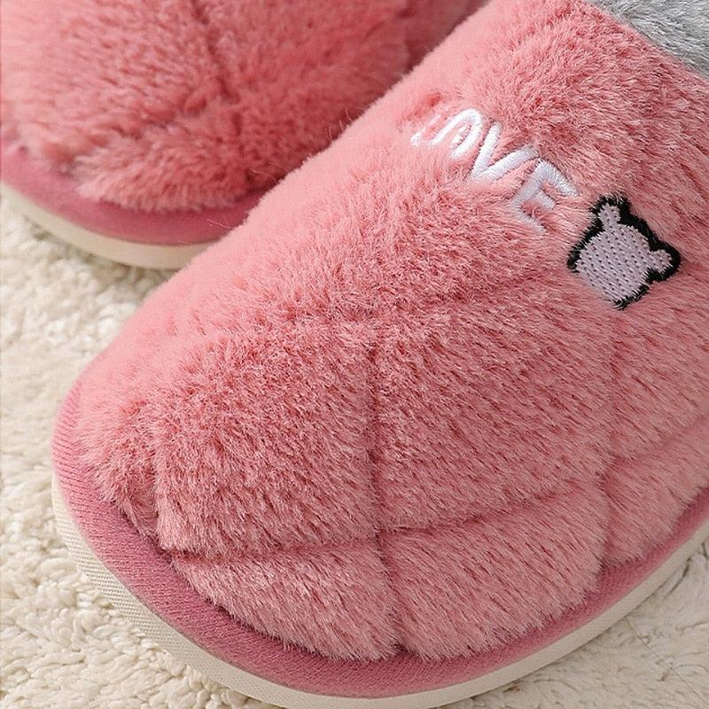 Pink fuzzy slip-on slippers with plush lining and small bear graphic on the toe
