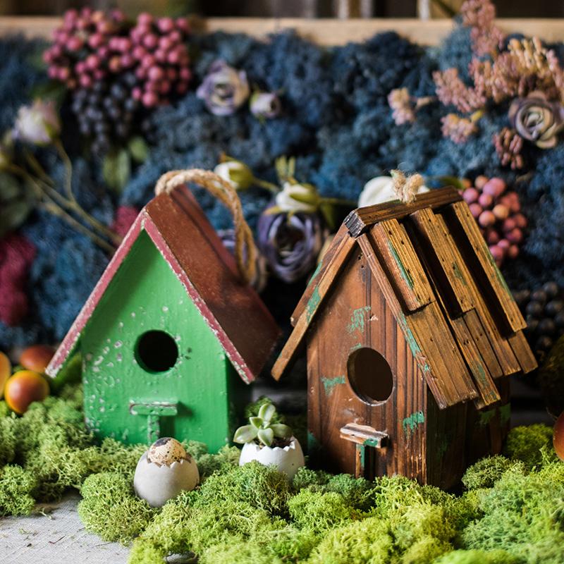 Wood birdhouse ornament display: green, brown, and teal houses on mossy grass.