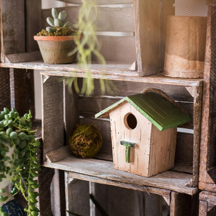 Wood birdhouse ornament with green roof and round entrance on a wooden shelf.