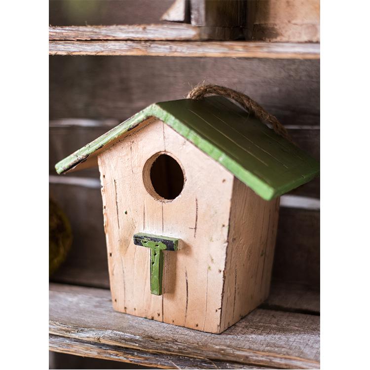 Close-up of cream wood birdhouse ornament with green roof and round entrance.
