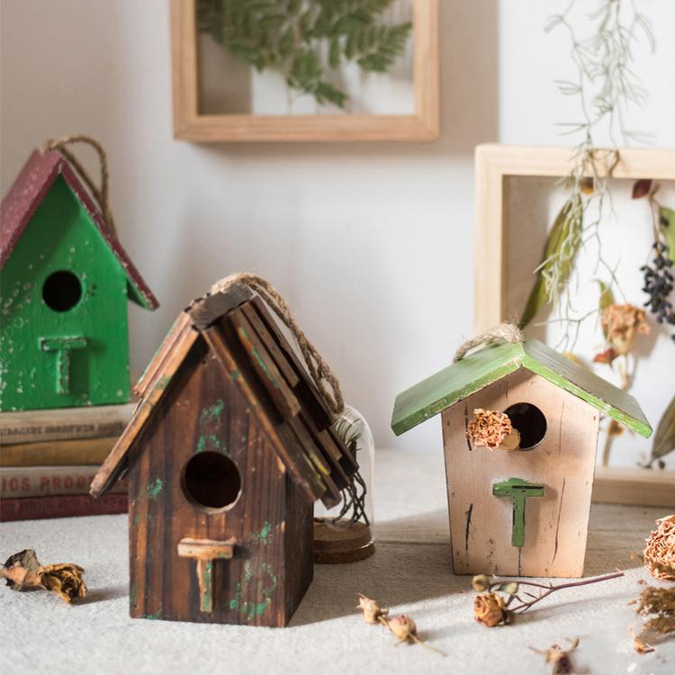 Two wood birdhouse ornaments, green and brown roofs, on tabletop with leaves.