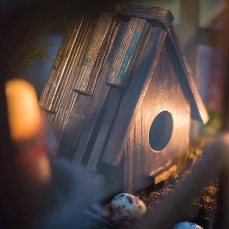 Wood birdhouse ornament with oval entrance hole and dark brown slatted roof.