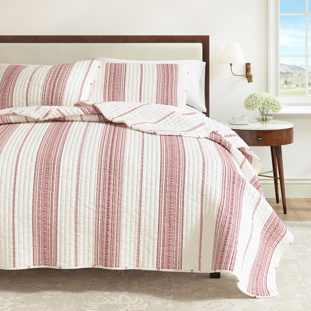Cream and red striped quilt draped over the bed edge with matching pillows