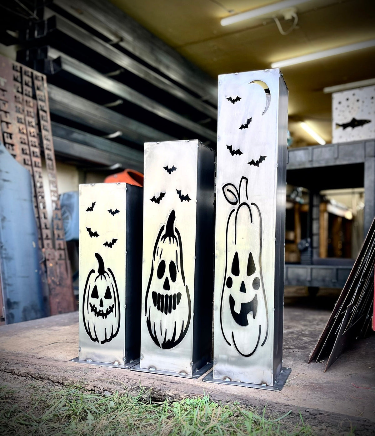 Three steel solar pillar lights with jack-o-lantern faces and bat icons in showroom