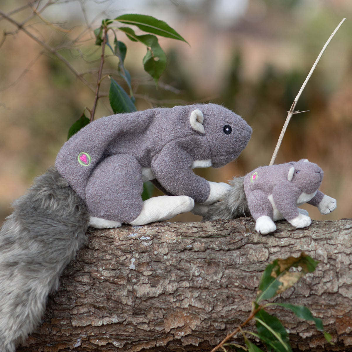 Gray-brown squirrel plush dog toy on a log with a small matching plush beside it